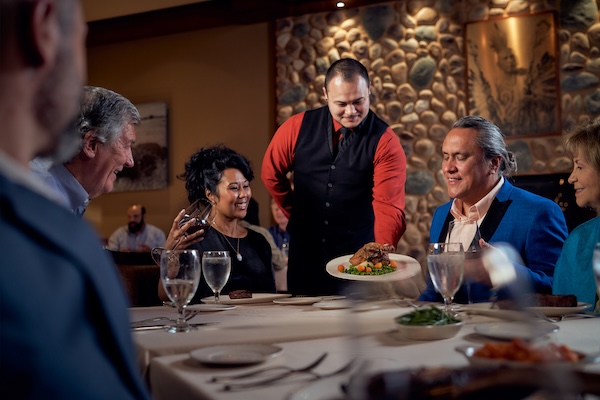 Waiter serving a table of smiling people at a steakhouse