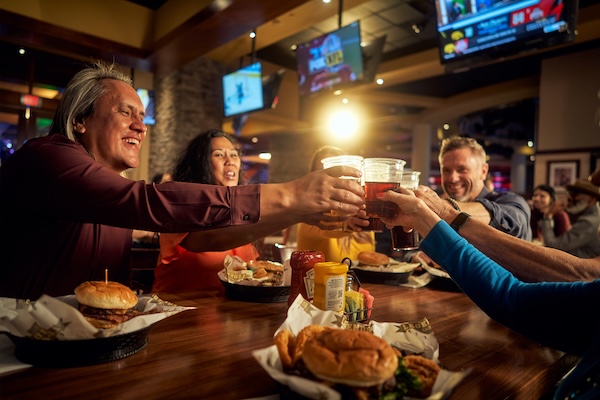 People smiling and cheersing with beers in a sports bar